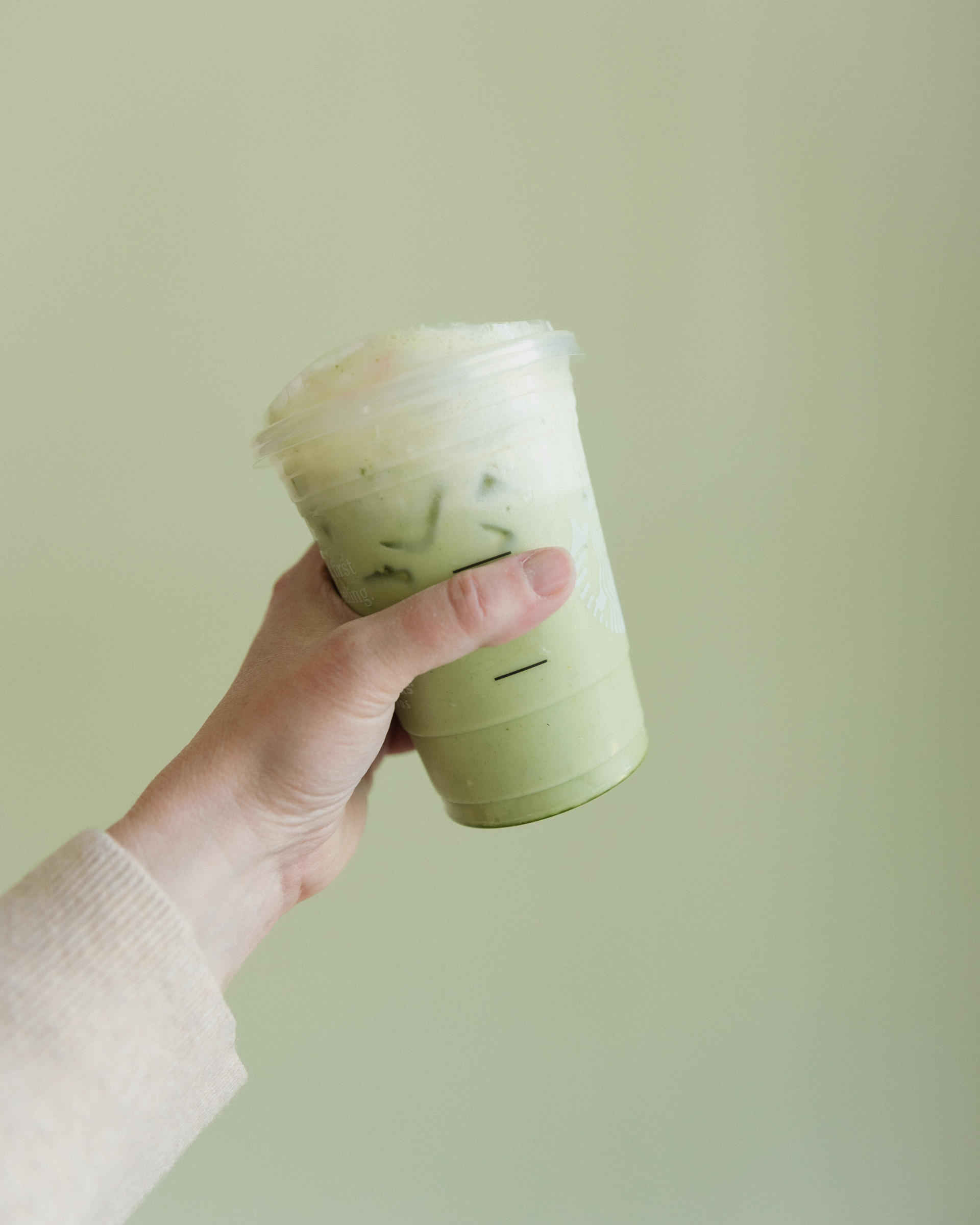 hand holding Starbucks cup with iced matcha latte in front of green wall