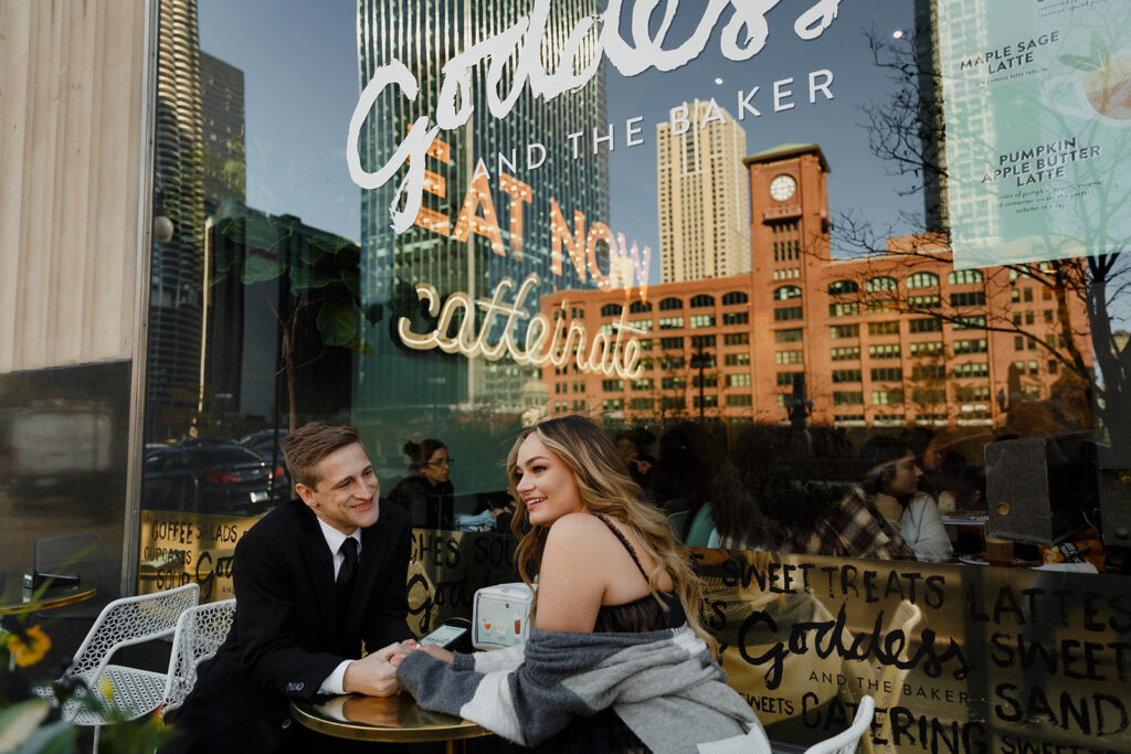 couple sitting in front of Goddess and the Baker on Wacker Drive with Riverwalk in reflection Romantic River North engagement session