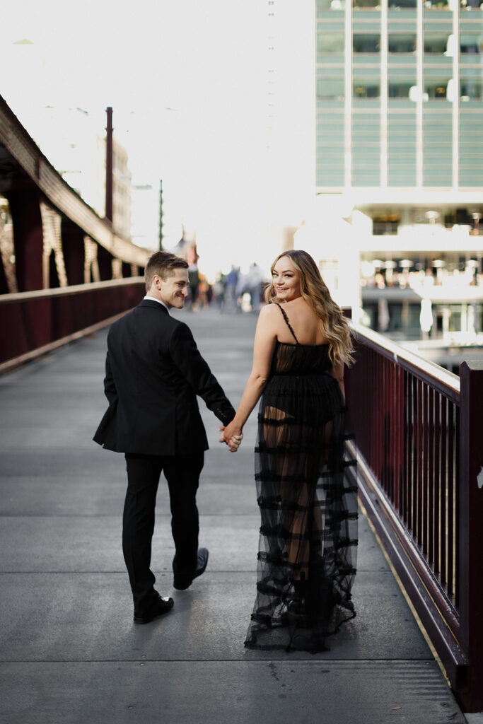 couple crossing Riverwalk Bridge with girl looking back Romantic River North engagement session